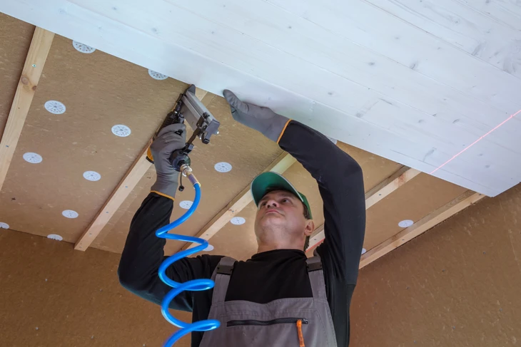 Ouvrier en tenue de travail installant de l'isolant thermique entre les chevrons d'une charpente