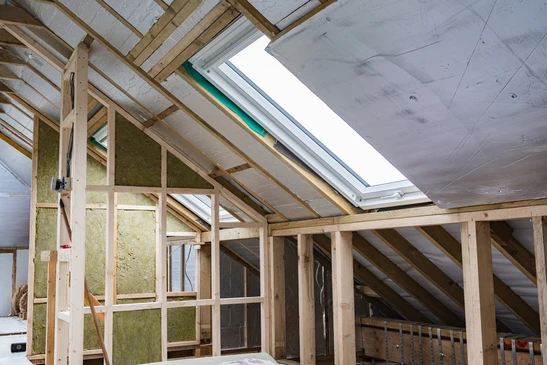 Chantier de r&eacute;novation de combles avec charpente bois apparente, isolation en laine min&eacute;rale verte entre chevrons