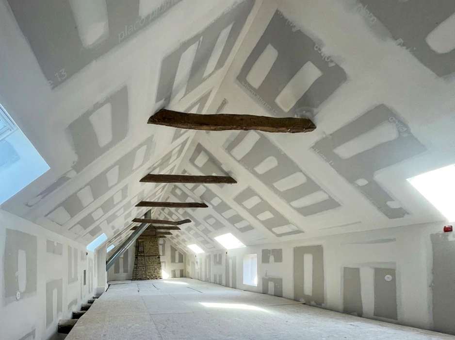 Combles aménagés en cours de finition avec escalier escamotable bois, cartons de déménagement et parquet flottant en cours de pose