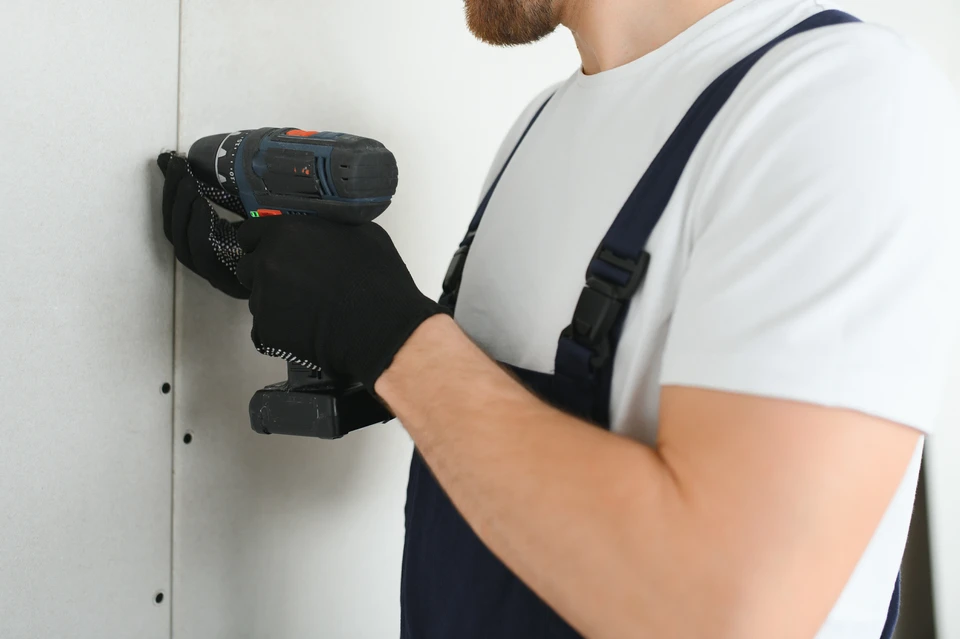 Photographie réelle d'un artisan plaquiste en action sur un chantier, appliquant de l'isolant thermique sur une paroi intérieure de mur avec precision et professionnalisme. L'isolant biosourcé ou minéral est visible, les outils et matériaux de plaquiste sont présents, et la scène capture le travail d'isolation intérieure murale dans une habitation en cours de rénovation, montrant le sérieux et la qualité du travail.