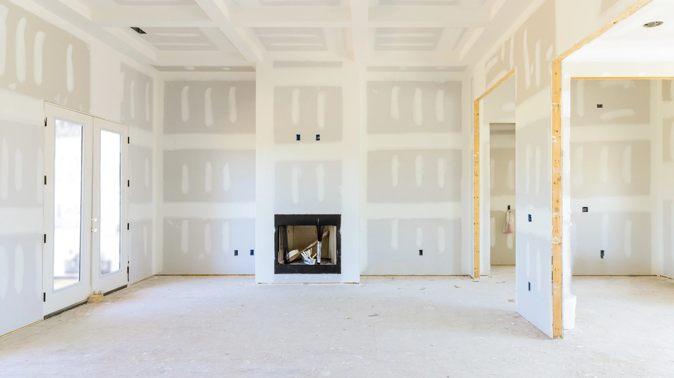 Ouvrier en bâtiment portant casque jaune de sécurité applique enduit de finition sur mur intérieur avec spatule