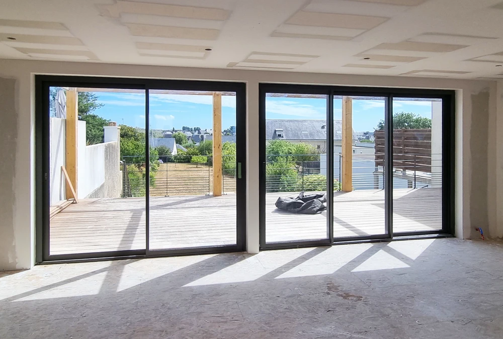Grenier en cours de rénovation, vaste espace sous combles avec parquet bois brut, mur en pierre apparente, charpente en bois exposée